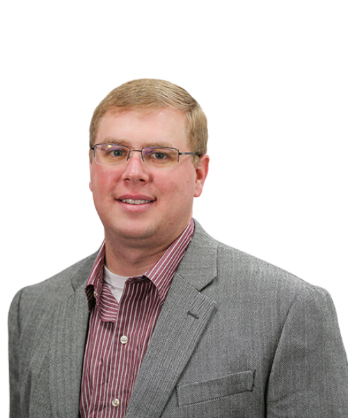 A man with short blond hair and glasses, specializing in revenue cycle management, is wearing a gray blazer over a red and white striped shirt. He is smiling and posed against a plain, light background.