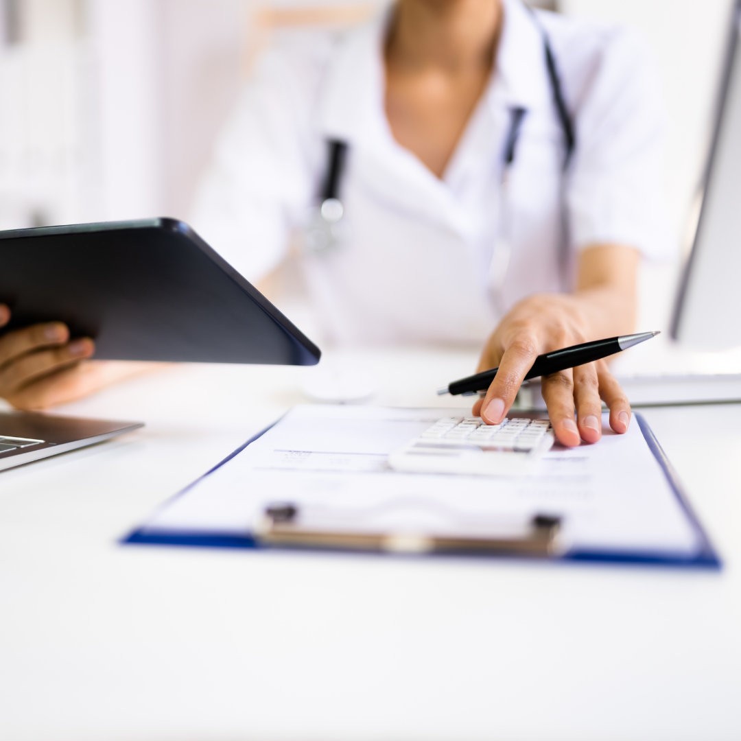 A doctor in a white coat sits at a desk, holding a digital tablet and pointing at a clipboard with documents. A stethoscope hangs around the doctors neck, ready to discuss Our Services.